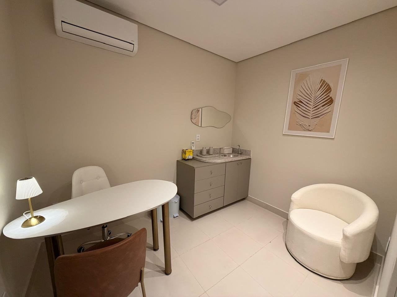 Sala 01: consultório com mesa oval, abajur, poltrona, bancada com pia e ar-condicionado